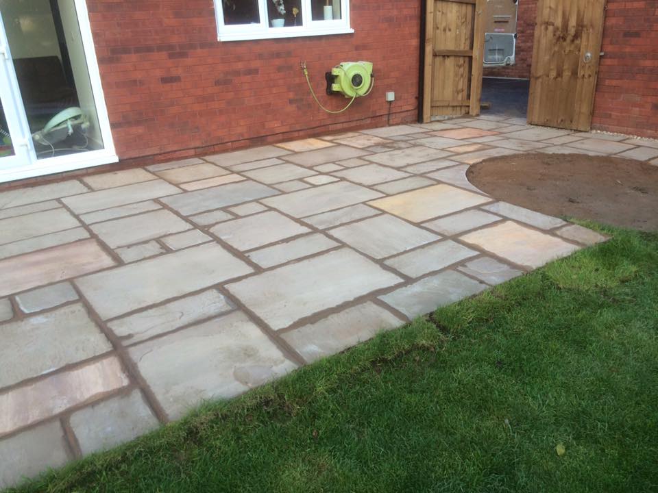 Sandstone patio and lawn laid by CJW against a red-brick house